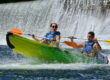 une femme et un homme à la sortie d'un tobboggan ou glissière sur l'ardèche à Sampzon, la femme est surprise par l'eau, le garçon sourit, derrière on aperçoit une chute, un bateau canoe jaune et vert une pagaie orang et une jaune