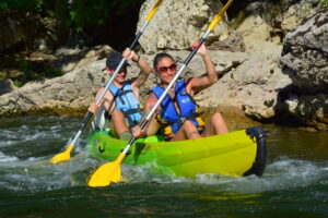 canoe jaune et vert avec un homme et une femme avec des pagaies et des gilets de sauvetages entrain de passer un rapide en canoe sur l'Ardèche
