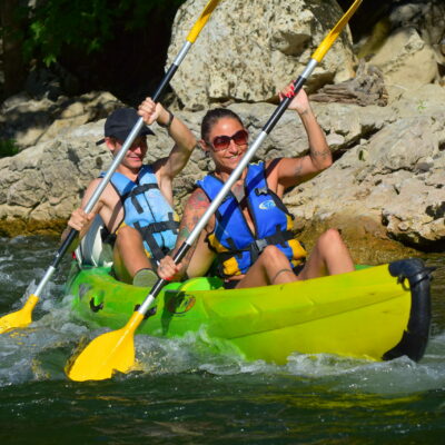 canoe jaune et vert avec un homme et une femme avec des pagaies et des gilets de sauvetages entrain de passer un rapide en canoe sur l'Ardèche