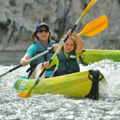 une femme et un enfant en canoe jaune et vert avec des gilets de sauvetage vert dans un rapide sur la rivière Ardeche
