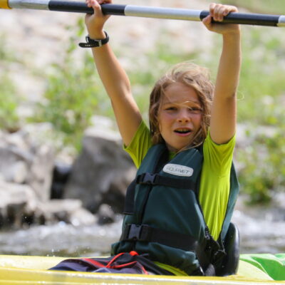 un enfant en canoe, leve les bras avec sa pagaie en l'air sur la riviere ardeche