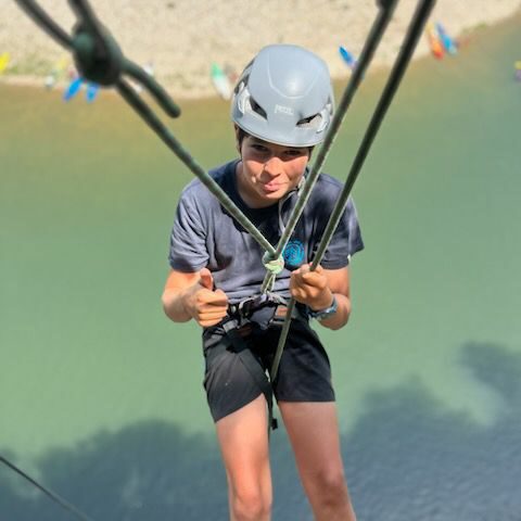 un adolescent descend en rappel au dessus de l'Ardèche, en dessous de lui la rivière, il porte un t-shirt element , un short et casque gris petzl