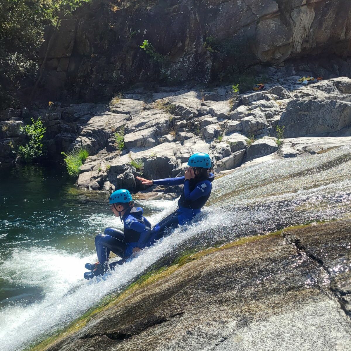 dans la ricère deux enfants en combinaisons néoprènes font du toboggan , ils portent des combinaisons néoprènes noires et bleues sealand et des casques bleus petzl