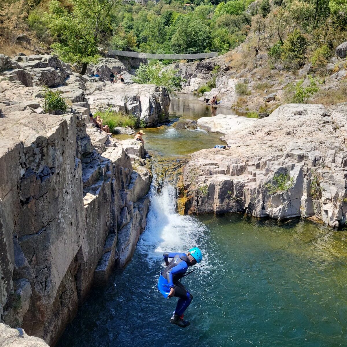 Un homme avec une combinaison néoprène et un casque en train de sauter dans la rivière