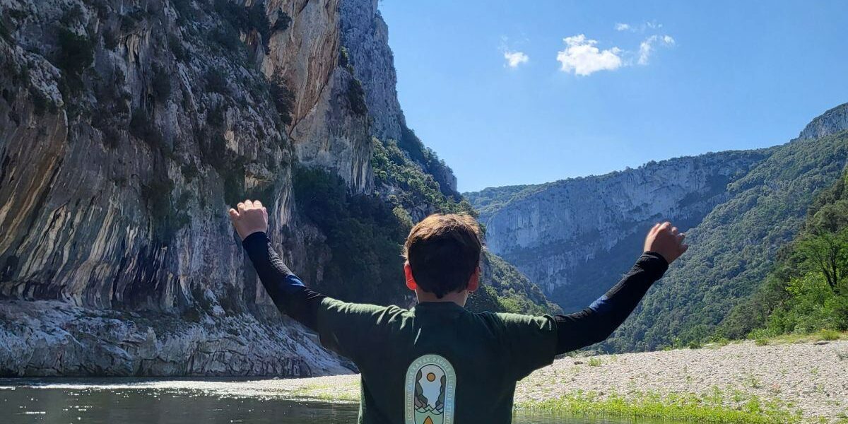 Paddle dans les Gorges de l’Ardèche Un enfant est debout de dos sur un paddle sur l'eau levant les 2 bras