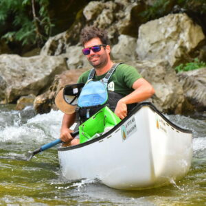 Un homme est sur un canoë. Il tient une pagaie et porte des lunettes de soleil