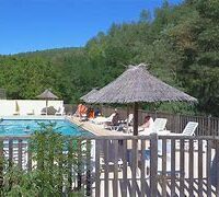 une barriere en bois, derrière des parasols en jonc autour d'une piscine sous le soleil, des bains de soleil autour de la piscine au milieu de la fôret.