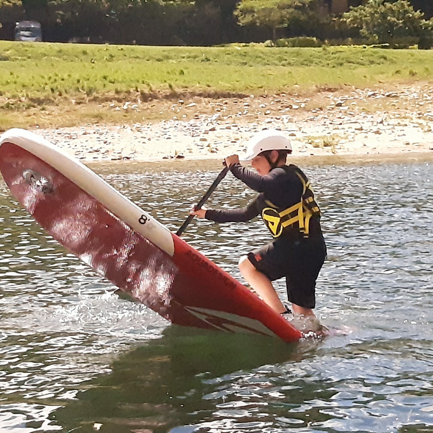 un enfant sur un paddle aquadesign 8' avec un casque blanc sweet, un gilet de sauvetage jaune et noir fait un efigure sur la rivière ardèche