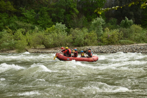 une famille dans un rafting, 2 adultes et 4 enfants un guide, le raft est rouge, ils sont dans des rapides sur la rivière Ardèche