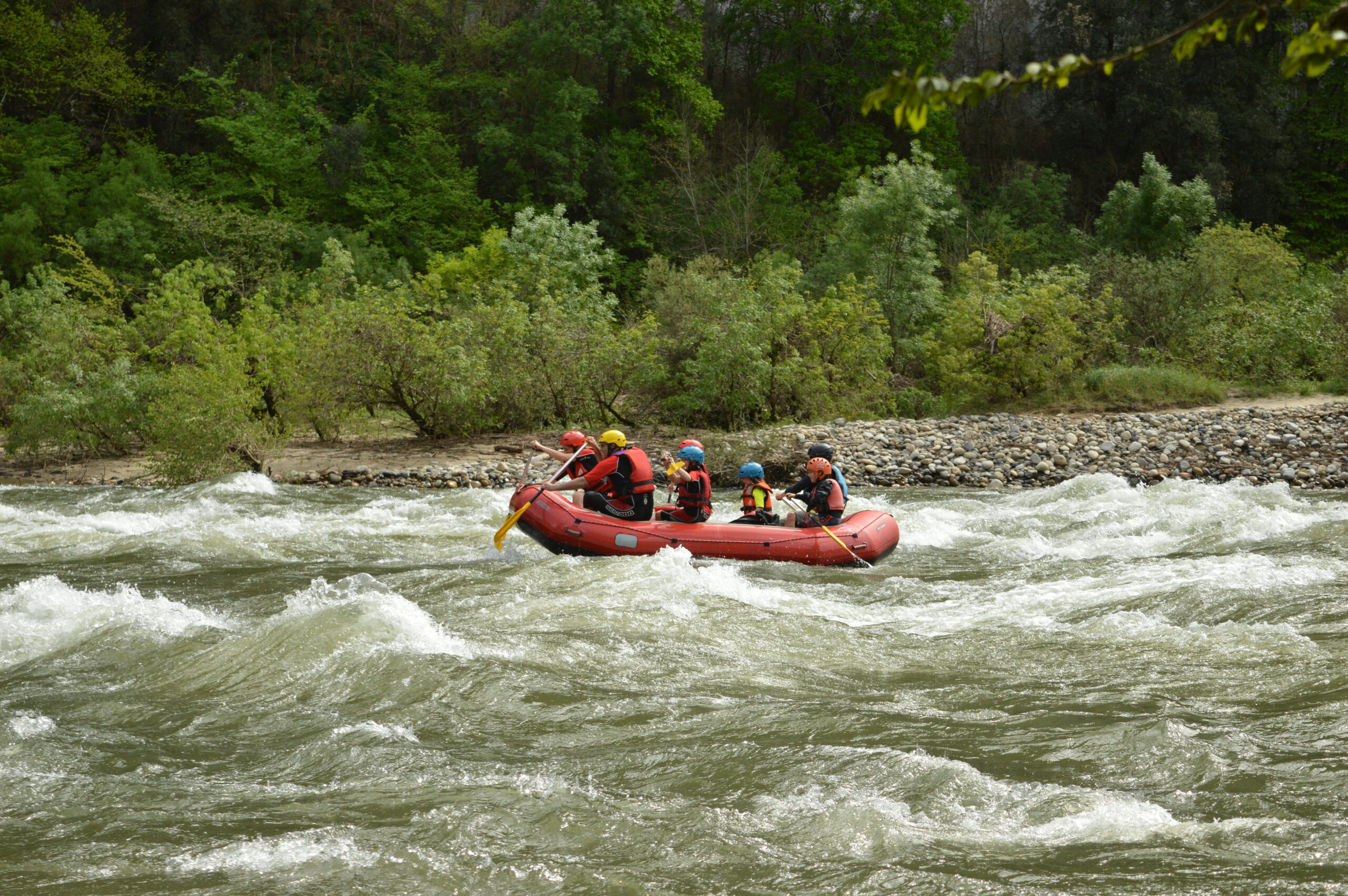 une famille dans un rafting, 2 adultes et 4 enfants un guide, le raft est rouge, ils sont dans des rapides sur la rivière Ardèche