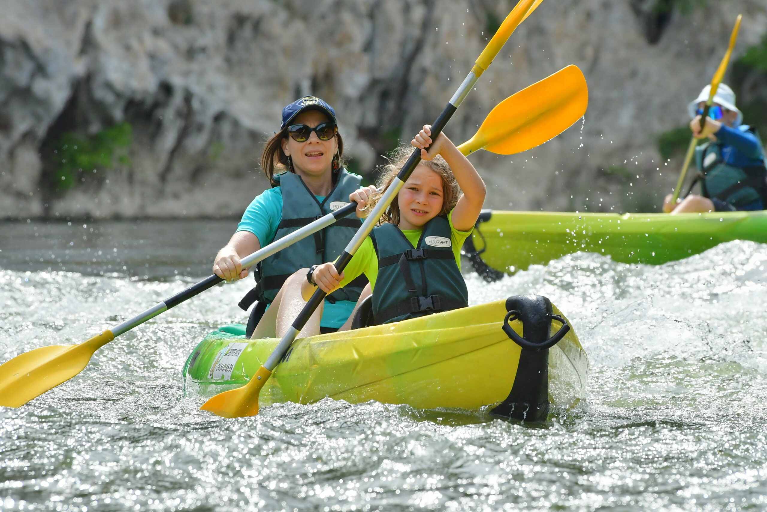 une femme et un enfant en canoe jaune et vert avec des gilets de sauvetage vert dans un rapide sur la rivière Ardeche au cours d'une descente en canoë sur jours