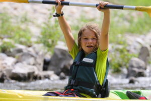 un enfant en canoe, leve les bras avec sa pagaie en l'air sur la riviere ardeche