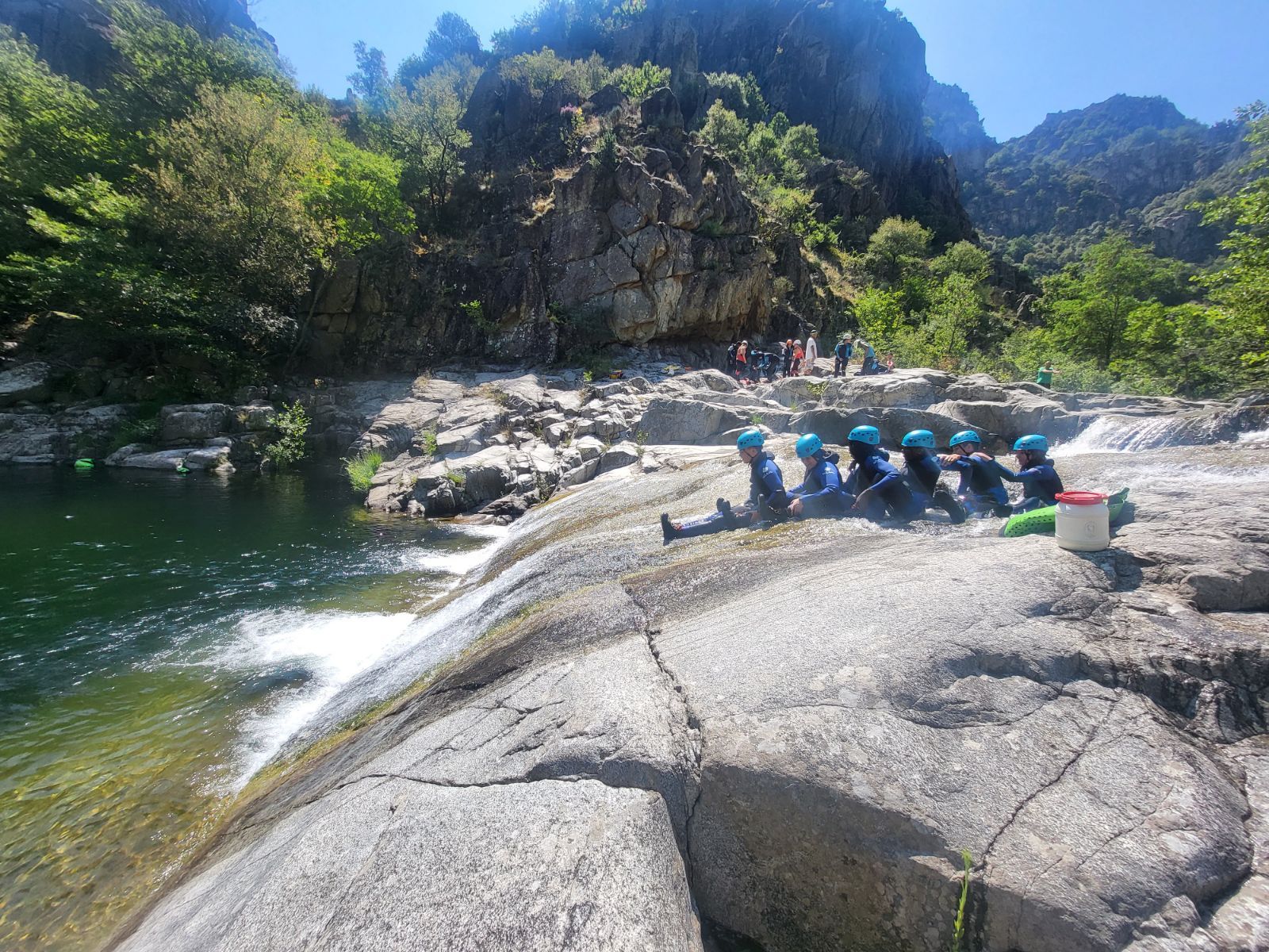 6 jeunes assis dnas la ricère vont faire un toboggan ils sont assis, ils portent des combinaisons néoprènes noires et bleues avec des casques bleus petzl