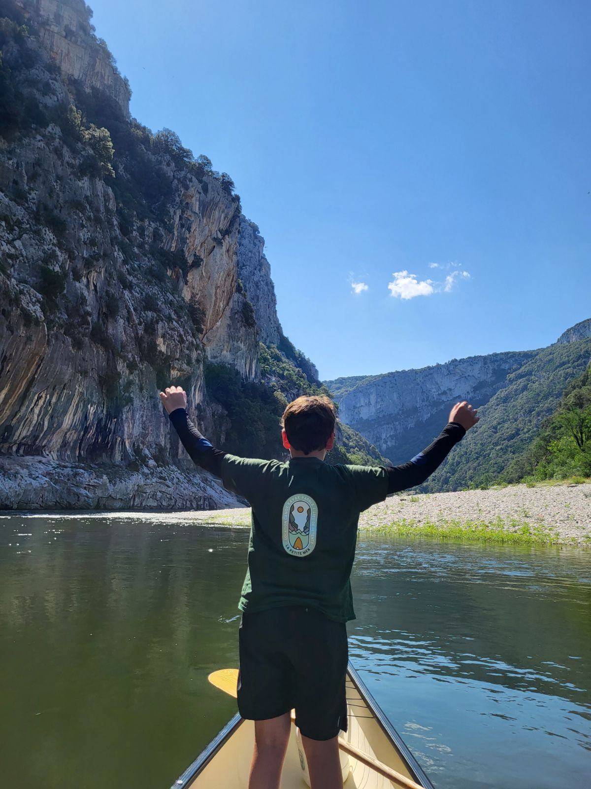 A child is standing with their back to the camera on a paddleboard on the water, raising both arms.