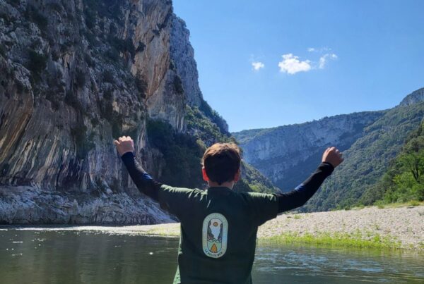 Un enfant est debout de dos sur un paddle sur l'eau levant les 2 bras
