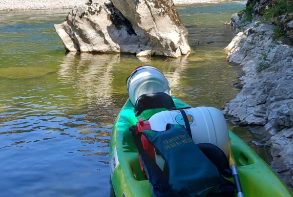 A yellow and green double canoe with two waterproof containers, a life jacket is placed on the canoe along with a paddle, the water is translucent, a rock in the middle of the river.