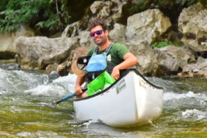 Un homme est sur un canoë. Il tient une pagaie et porte des lunettes de soleil