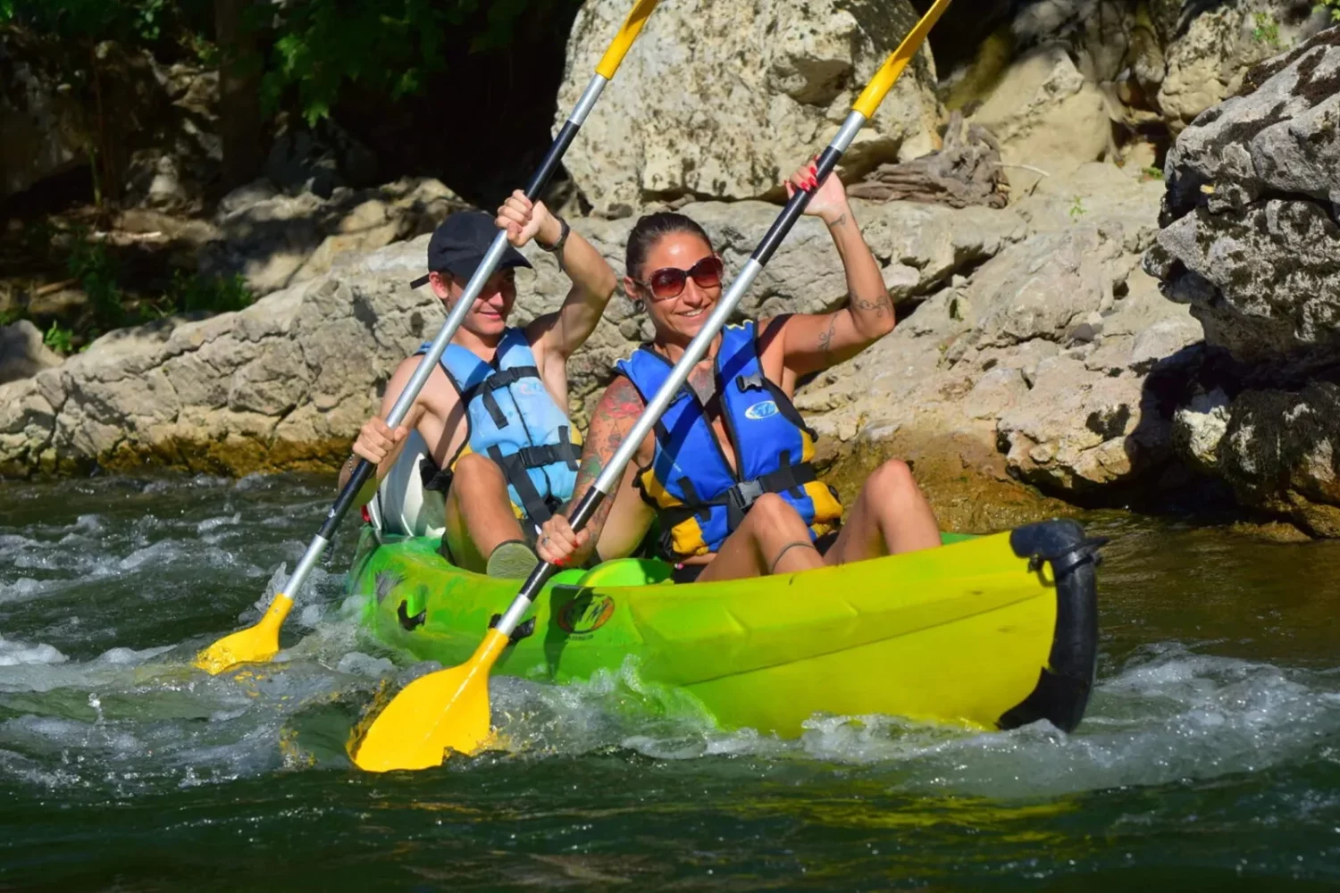 un homme et une femme dans un bateau  canoë kayak jaune et vert sur la rivière Ardèche